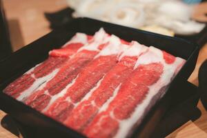 schließen oben viele Rindfleisch Scheiben im schwarz Tablett auf Tisch. foto