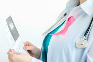 Frau Arzt mit Rosa Band auf Weiß medizinisch Uniform hält Ergebnisse von Ultraschall Scan im ihr Hände. Brust Krebs Bewusstsein Monat Symbol. foto