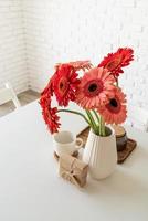 helle Gerbera-Gänseblümchen in weißer Vase auf Küchentisch mit Geschenkbox foto