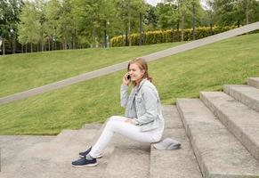 Frau, die auf ihrem Handy eine SMS schreibt und auf der Treppe im Park sitzt foto