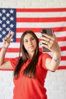 schöne frau, die ein selfie auf dem hintergrund der usa-flagge macht