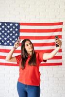 schöne frau, die ein selfie auf dem hintergrund der usa-flagge macht