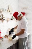 Koch mit Weihnachtsmütze kocht ein Dessert in der Küche Abwischen der Sahne foto