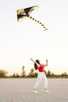 junge Frau, die bei Sonnenuntergang einen Drachen in einem öffentlichen Park fliegt
