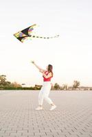 junge Frau, die bei Sonnenuntergang einen Drachen in einem öffentlichen Park fliegt