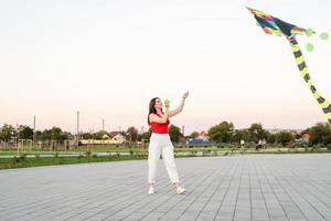 junge Frau, die bei Sonnenuntergang einen Drachen in einem öffentlichen Park fliegt foto