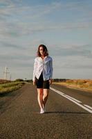 Frau in weißem Hemd geht die Straße entlang zwischen den Feldern