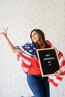 Frau mit amerikanischer Flagge, die Brieftafel mit den Worten glücklicher Unabhängigkeitstag hält und Friedenszeichen zeigt foto