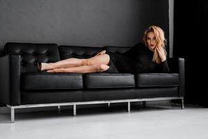 schönes Mädchen im schwarzen Kleid liegt auf der Couch foto