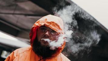 ein Mann mit Schutzbrille und orangefarbenem Anzug. Mann atmet Rauch aus foto