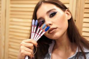 Mädchen mit blauem Make-up bedeckt ihr Gesicht mit einer Palette mit Nägeln foto
