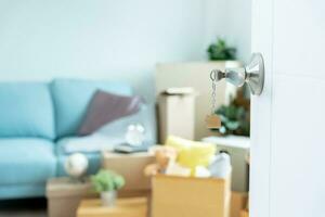 Umzug, Umzug. Der Schlüssel wurde in die Tür des neuen Hauses gesteckt, im Zimmer befand sich ein Karton mit persönlichen Gegenständen und Möbeln. in die Wohnung oder Eigentumswohnung einziehen foto