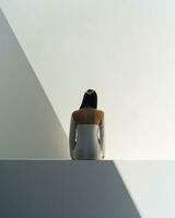ein fesselnd Nebeneinander von Licht und Schatten ein Frau sitzend auf ein rein Weiß Wand, ihr Silhouette Hinzufügen Tiefe zu das Szene.. generativ ai foto