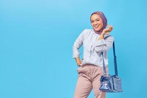 fröhliche junge Frau, die eine Tasche auf blauem Hintergrund hält