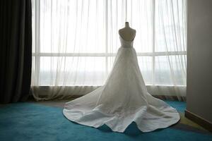 schön Weiß Hochzeit Kleid auf ein Weiß Mannequin im das Zimmer mit groß Fenster foto