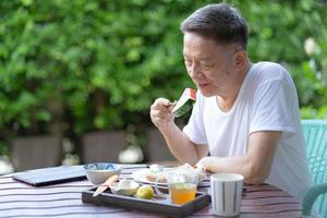 reifer Mann, der gesundes Frühstück im Garten isst