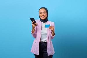 fröhliche asiatische frau, die kreditkarte zeigt und handy hält foto