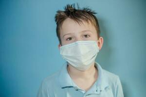Junge im medizinisch Maske auf Blau Hintergrund. Kind mit Grippe, Grippe oder kalt geschützt von Viren, Verschmutzung im Schlecht Epidemie Situation, unter Patienten mit Coronavirus foto