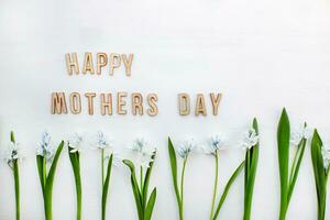 frisch Blau Frühling Blumen Scilla Sibirien und hölzern Tafel mit Stichprobe Text glücklich Mütter Tag Weiß Tisch. foto