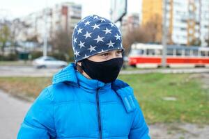 Junge im schwarz Gesicht Maske auf Straße in der Nähe von Straßenbahn im Ukraine. Coronavirus Epidemie. Gesicht Maske gegen Virus, krank, Epidemie, Grippe. Coronavirus. Gesicht Maske zum Schutz Coronavirus Ausbruch foto