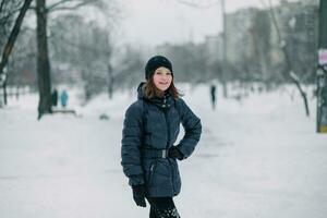 ein Mädchen mit ein Hand auf ihr Gürtel. ein Kind auf ein schneebedeckt Straße im das Stadt. Stadt nach Schneefall. foto