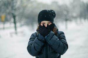 Mädchen bedeckt Mund mit Handschuhe. das Mädchen gemacht ein Geste, Schweigen. ein Kind Spaziergänge nach Schule auf das Straße im ein Schneefall. foto
