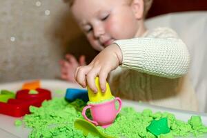 Baby hält Schimmel zum spielen mit Sand beim heim. lehrreich Spielzeuge zum Kinder oben zu Jahr. Mädchen Theaterstücke mit kinetisch Sand. Kind baut Hirten im bilden von Briefe von Sand. früh Entwicklung von Kinder. foto