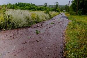 Streams von Wasser fließend entlang das ländlich Straße. Flut nach das Regen. foto