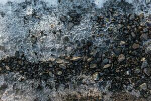 Schnee Startseite und Eis auf das gefroren Boden mit Steine und Sand. Schnee auf ein Felsen. Winter Hintergrund foto