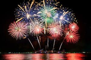 erstaunliches schönes buntes Feuerwerk in der Feiernacht, das am Meeresstrand mit mehrfarbiger Reflexion auf dem Wasser gezeigt wird foto