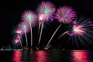 erstaunliches schönes buntes Feuerwerk in der Feiernacht, das am Meeresstrand mit mehrfarbiger Reflexion auf dem Wasser gezeigt wird foto