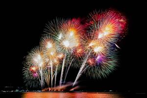 erstaunliches schönes buntes Feuerwerk in der Feiernacht, das am Meeresstrand mit mehrfarbiger Reflexion auf dem Wasser gezeigt wird foto