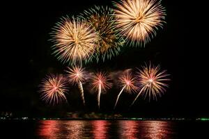 erstaunliches schönes buntes Feuerwerk in der Feiernacht, das am Meeresstrand mit mehrfarbiger Reflexion auf dem Wasser gezeigt wird foto