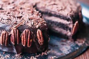 Makroansicht des köstlichen dunklen Schokoladenkuchens mit Chips, schönem Zuckerguss und Pekannüssen auf der Seite auf der Metallschale. selektiver Fokus. luxuriöse Glasur. Bild für Speisekarte oder Süßwarenkatalog foto