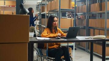 asiatisch Frau mit Behinderung Arbeiten im Lagerhaus, tun Büro Arbeit zum Lager Logistik und Inventar auf Laptop. weiblich Rollstuhl Benutzer Planung Lager Verteilung im Behinderung freundlich Depot. foto