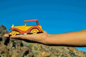 ein Person halten ein Spielzeug Auto im Vorderseite von ein Berg foto