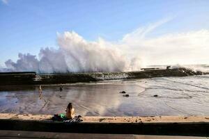 ein Frau Sitzung auf das Strand Aufpassen ein Welle Absturz foto