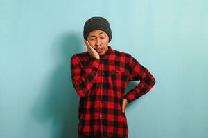 unzufrieden jung asiatisch Mann halten seine Wange Leiden von Zahnschmerzen, isoliert auf Blau Hintergrund foto