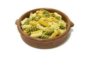 Spiral- Pasta von drei Farben, serviert im ein Lehm Schüssel. isoliert auf ein Weiß Hintergrund. Vegetarier Essen Konzept. foto