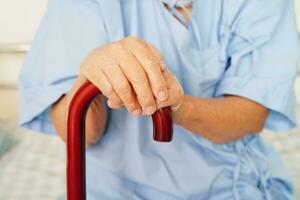 asiatisch Alten Behinderung Frau geduldig halten Gehen Stock im faltig Hand beim Krankenhaus. foto