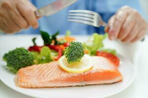 asiatisch Alten Frau geduldig Essen Lachs Anteil und Gemüse Salat zum gesund Essen im Krankenhaus. foto