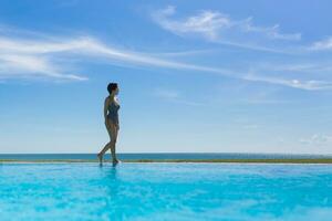 schön Frau im ein Schwimmen passen Gehen um das Kante von das Schwimmbad auf Urlaub. foto