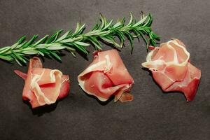 Stücke von getrocknet Schweinefleisch Jamon Prosciutto mit Rosmarin auf ein schwarz Tafel foto