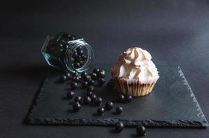 Muffin mit Johannisbeeren auf schwarzem Hintergrund und verstreuten Beeren. foto
