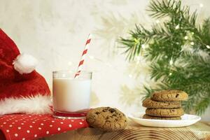 Weihnachten Komposition. Milch zum Weihnachtsmann. Glas Milch, Kekse, Santa Hut, Tanne Zweig, Weihnachten Beleuchtung. foto