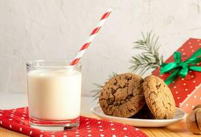 Milch zum Weihnachtsmann. Glas Milch mit festlich Trinken Stroh, Kekse, rot Polka Punkt Serviette und Geschenk Kasten. foto