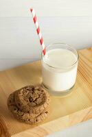 Milch im Glas, weiß Rot Trinken Stroh, Kekse auf hölzern Tafel auf Weiß. Weihnachten Milch zum Weihnachtsmann. foto