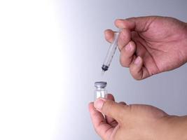 Die Hand eines Mannes hält eine Flasche Impfstoff und eine Schlinge zur Injektion.