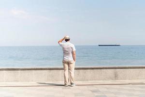 junger Mann in Sommerkleidung steht auf einem Pier, Meer im Hintergrund foto