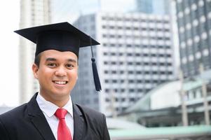 glücklicher Absolvent. glücklicher Asain-Mann in Abschlusskleidern mit Diplom foto